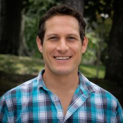 Headshot of Brian Yellen wearing a blue plaid shirt in front of woodland background